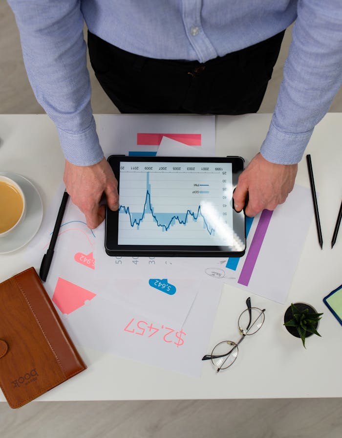 Top view of a professional analyzing financial data on a tablet at a desk.